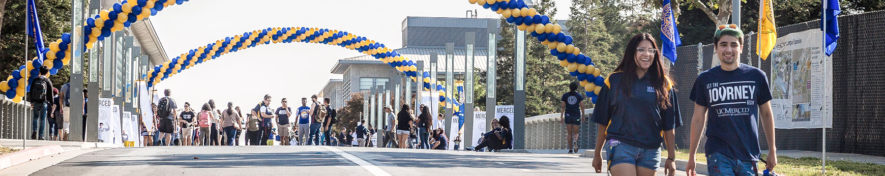 female and male student walking under an archway of balloons across scholars bridge