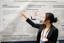 UC Tech 2025 poster presenter raises their right arm to point at a section of their poster board.