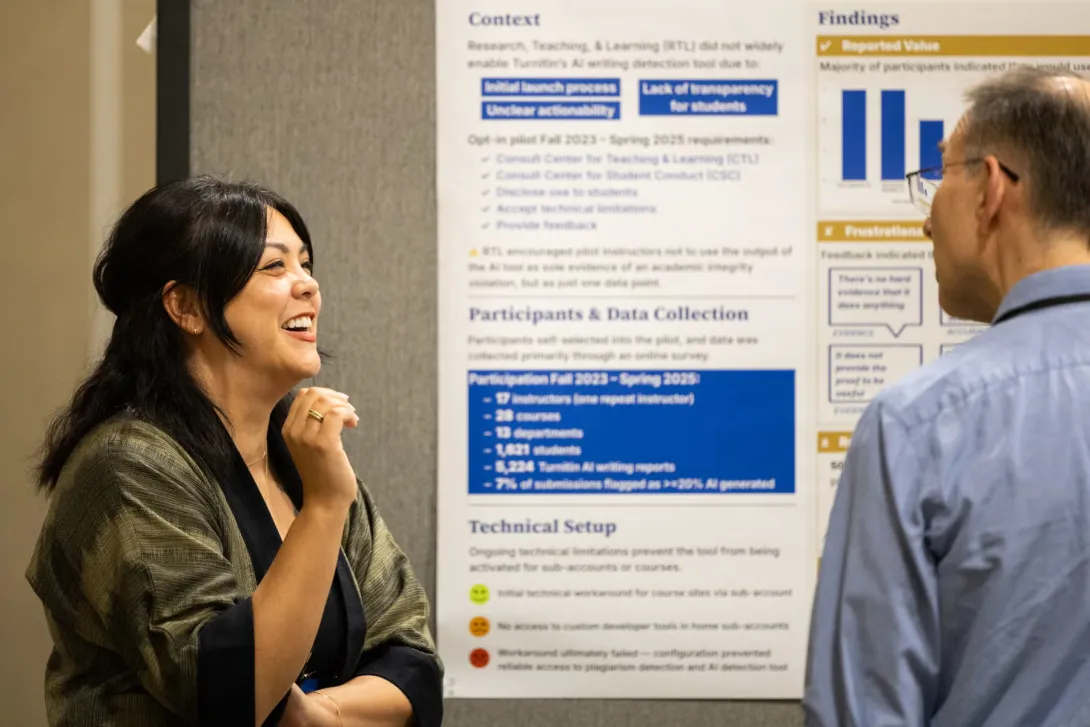 A UC Tech 2025 poster presenter speaks with an attendee about their poster, which is displayed in the background.
